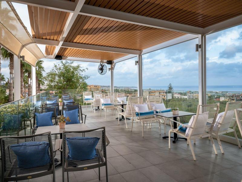 Przykryty taras z stołami i krzesłami, widok na morze i niebo