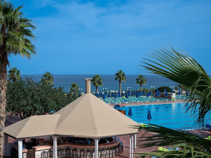 Duży basen z parasolami i palmami pod niebieskim niebem przy morzu