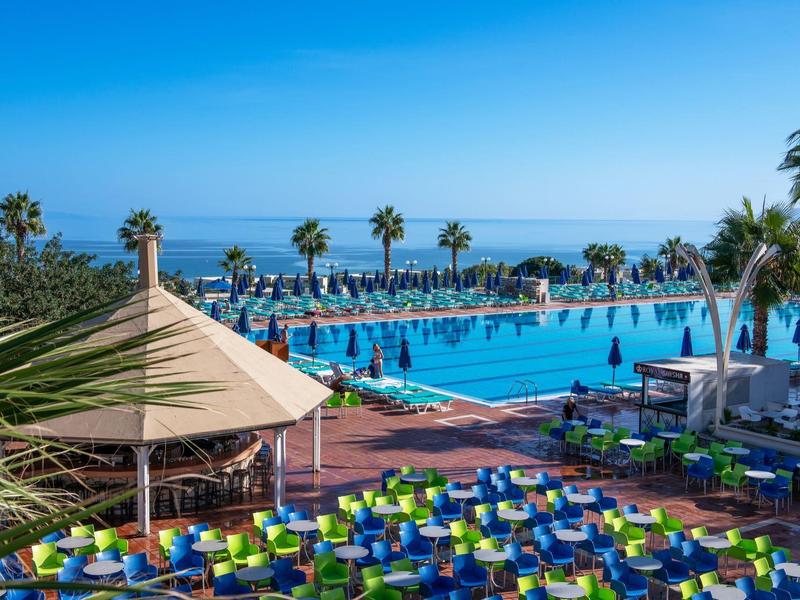 Duży basen na zewnątrz z leżakami i palmami pod czystym niebieskim niebem nad morzem