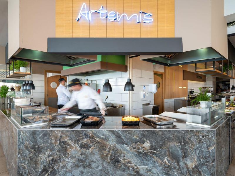 Nowoczesna kuchnia hotelowa z kucharzem, marmurowymi blatami i napisem Artemis.