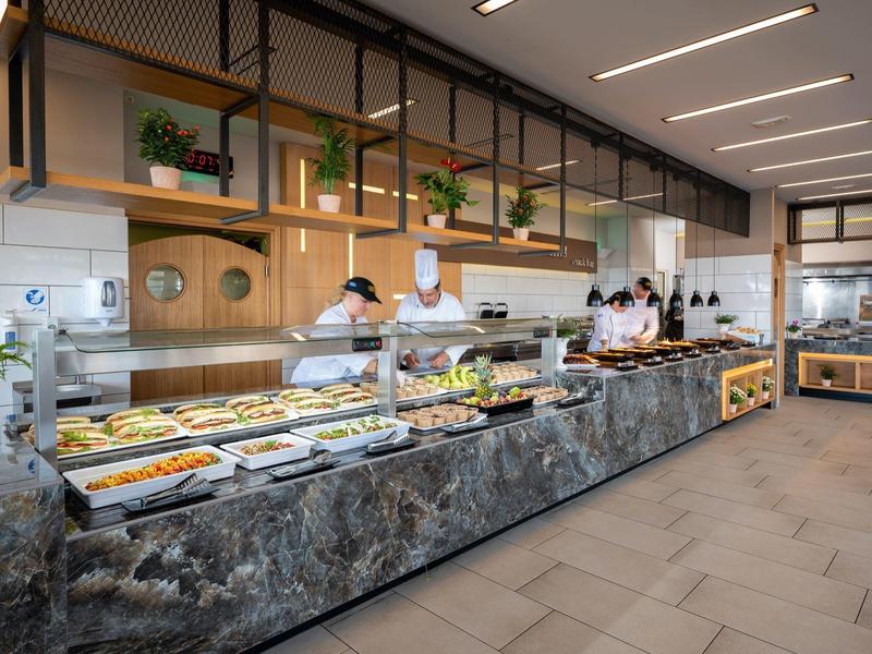 Nowoczesny bufet z różnorodnymi potrawami w jasnej restauracji z marmurowym kontuarem i roślinami.