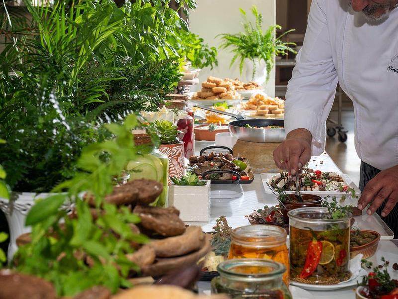 Kucharz dekoruje talerze przy bufecie z świeżymi składnikami i roślinami w tle.