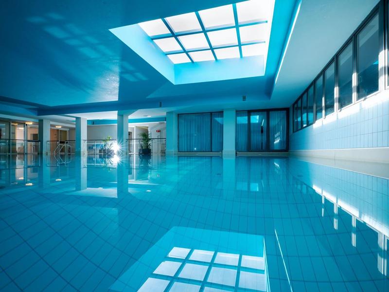 Wnętrze hotelu z dużym oświetlonym basenem i szklanym sufitem.