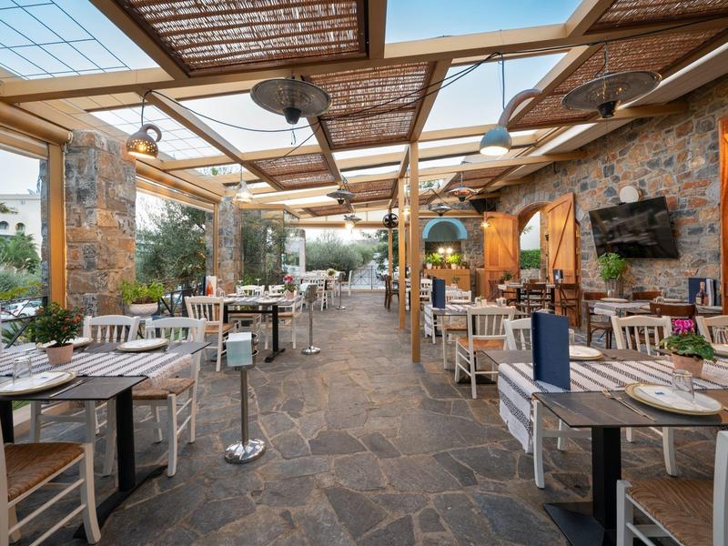 Otwarta restauracja z drewnianymi stołami i krzesłami, kamienną podłogą i szklanym dachem