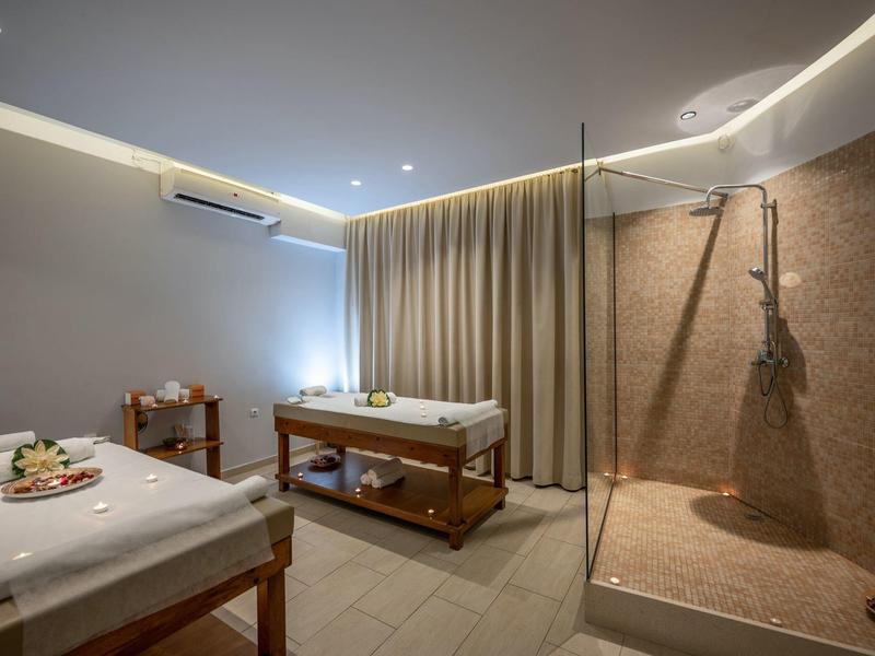 Nowoczesny pokój spa z dwoma stołami do masażu i prysznicem, ciepłe oświetlenie.