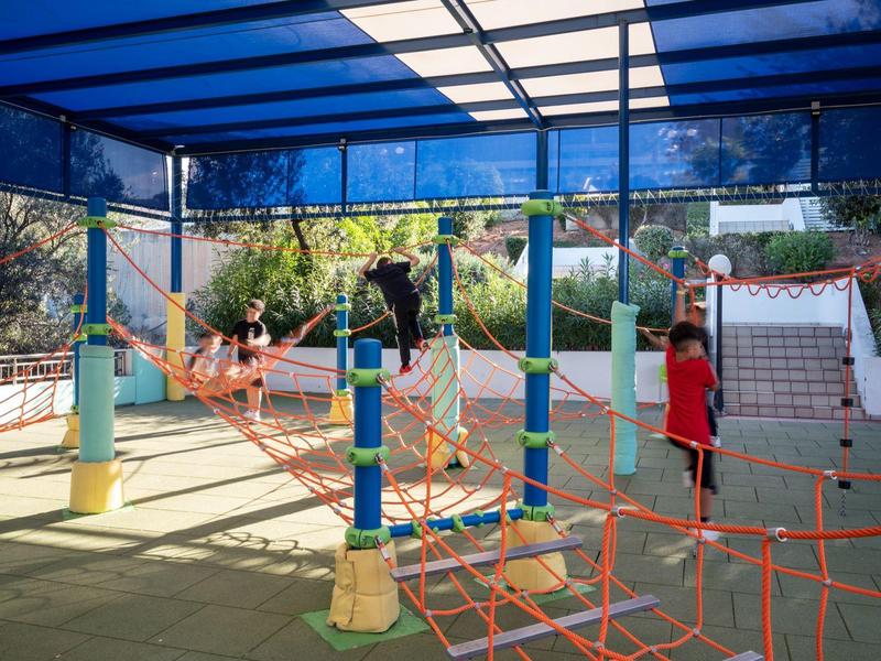 Zadaszony plac zabaw na zewnątrz dla dzieci z konstrukcją do wspinaczki i kolorowymi słupami.