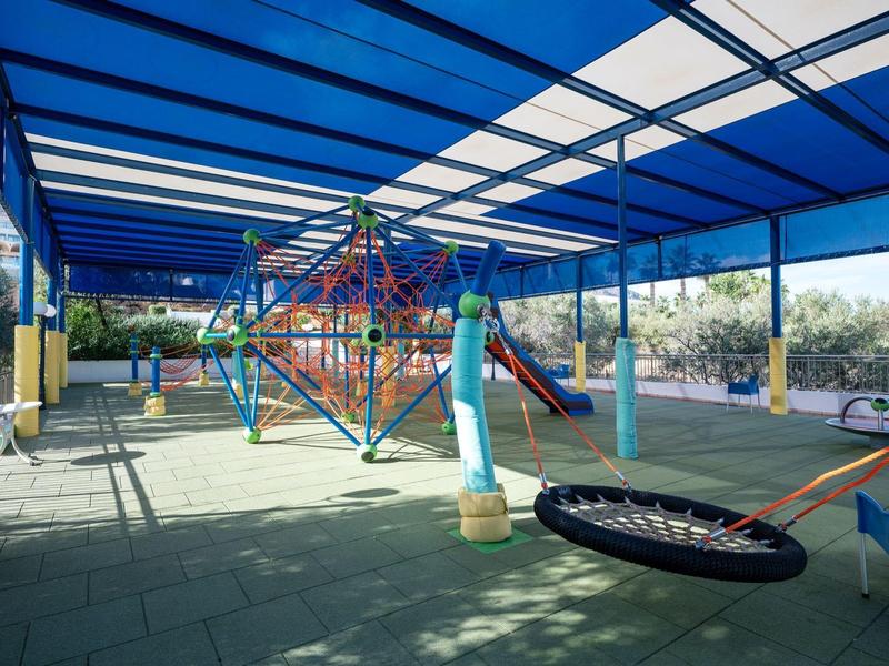 Zadaszony plac zabaw z siatką do wspinaczki, zjeżdżalnią i huśtawkami w hotelu