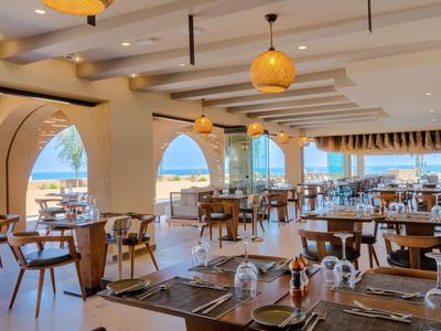 Světla restaurace s výhledem na moře, prostřené stoly a dřevěné židle.