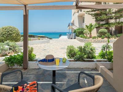 Terraza con sillas y mesa, vista al jardín, playa y mar con cielo despejado.