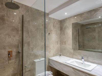 Baño moderno con paredes de mármol, bañera grande, ducha y espejo iluminado.