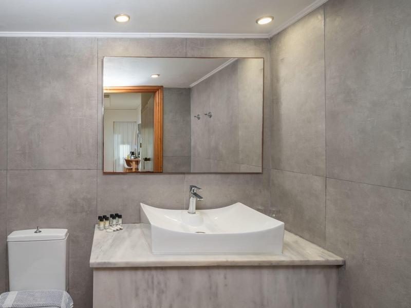Baño moderno con azulejos grises, lavabo blanco y espejo cuadrado.