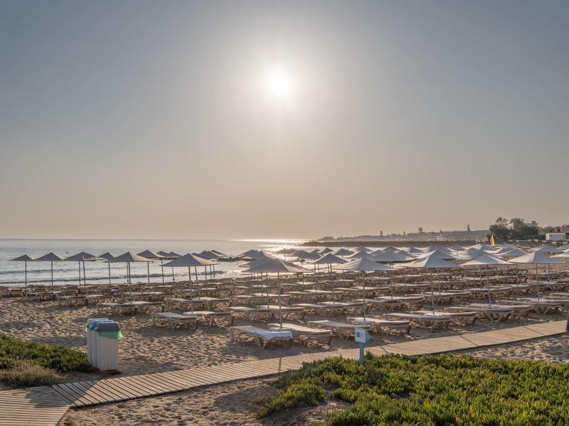 Playa con sombrillas y tumbonas al atardecer junto a un mar tranquilo.