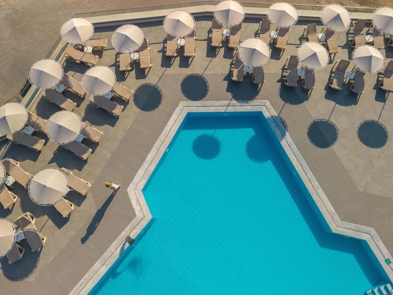 Vista aérea de una piscina al aire libre rodeada de sombrillas y tumbonas en una terraza pavimentada.