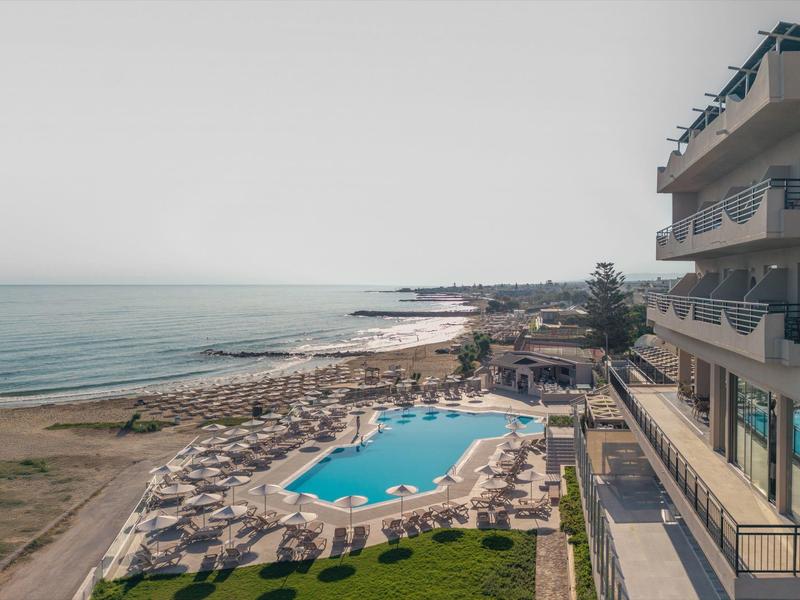 Complejo hotelero con piscina y sombrillas en la playa junto a tranquila costa marina.