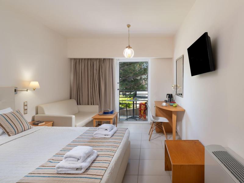 Habitación de hotel moderna con cama doble, escritorio, televisor y balcón con vista al jardín.