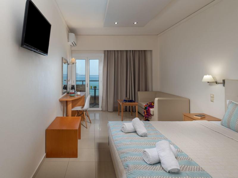 Habitación de hotel luminosa con cama doble, televisión, escritorio y balcón con vista al mar.