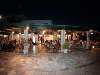 Beleuchtete Terrasse eines Restaurants mit Tischen und Gästen bei Nacht.