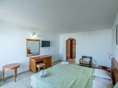 Hell eingerichtetes Hotelzimmer mit Doppelbett, TV, Holzmöbeln und Fliesenboden.