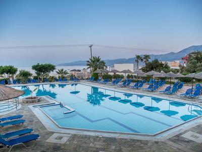Großer Außenpool mit blauen Liegestühlen, Sonnenschirmen und Blick auf das Meer und Berge.