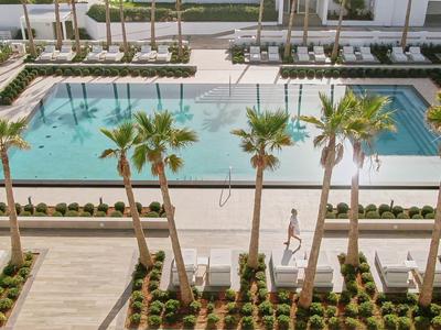 Widok na basen z palmami i leżakami obok hotelu.