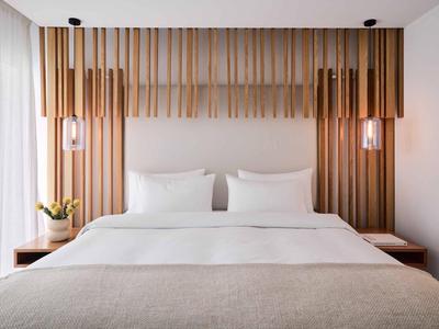 Nowoczesny pokój hotelowy z łóżkiem podwójnym, drewnianym zagłówkiem i dwoma lampami wiszącymi.