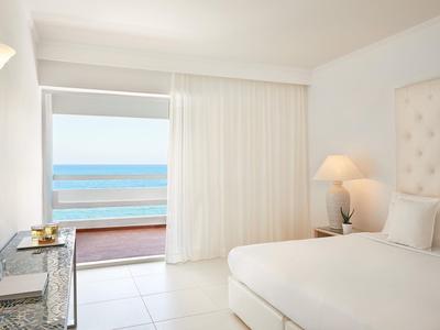 Jasny pokój hotelowy z dużym łóżkiem, widokiem na morze i dostępem do balkonu.