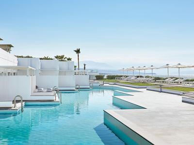 Area piscina moderna con sedute bianche e lettini sotto un cielo azzurro.