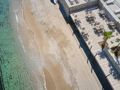 Widok z powietrza na piaszczystą plażę obok tarasu z stołami i krzesłami przy hotelu nad morzem