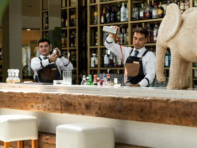 Due bartender preparano bevande in un bar d'hotel moderno con bancone in legno.