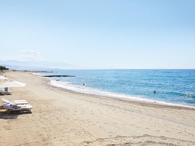 Szeroka piaszczysta plaża z leżakami wzdłuż wybrzeża pod bezchmurnym niebem