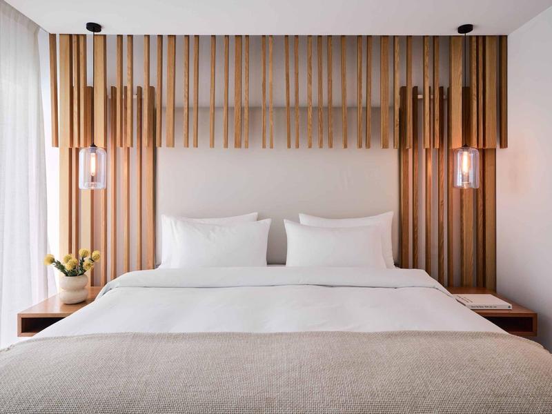 Nowoczesny pokój hotelowy z łóżkiem podwójnym, drewnianym zagłówkiem i dwoma lampami wiszącymi.