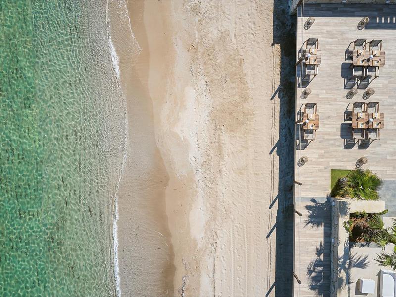 Widok z lotu ptaka na piaszczystą plażę z czystą wodą i sąsiednim drewnianym tarasem z miejscami do siedzenia.