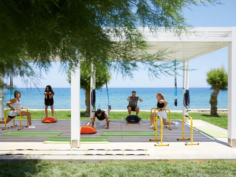 Zewnętrzny teren hotelowy z urządzeniami fitness nad morzem pod białym pawilonem.