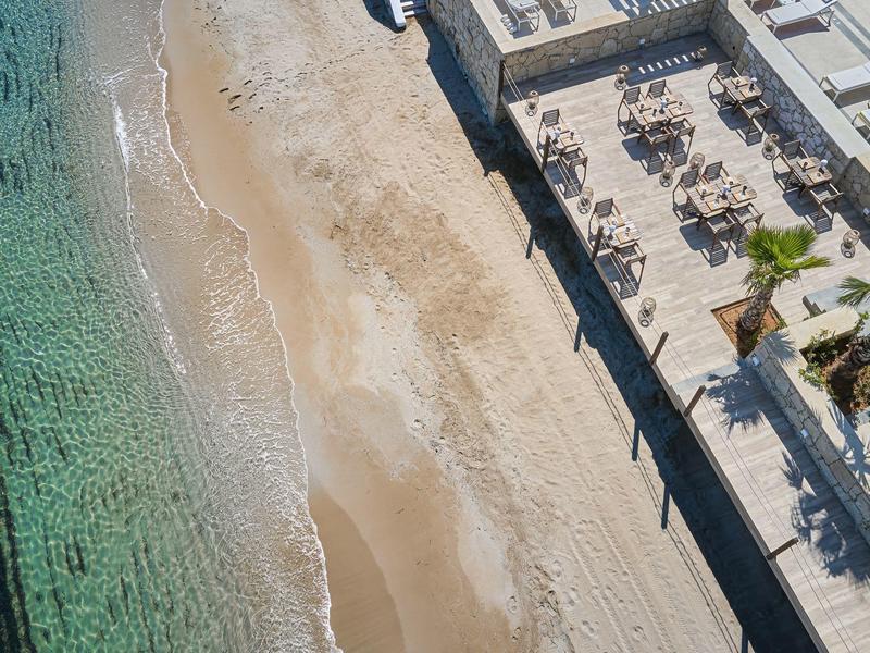 Widok z powietrza na piaszczystą plażę obok tarasu z stołami i krzesłami przy hotelu nad morzem