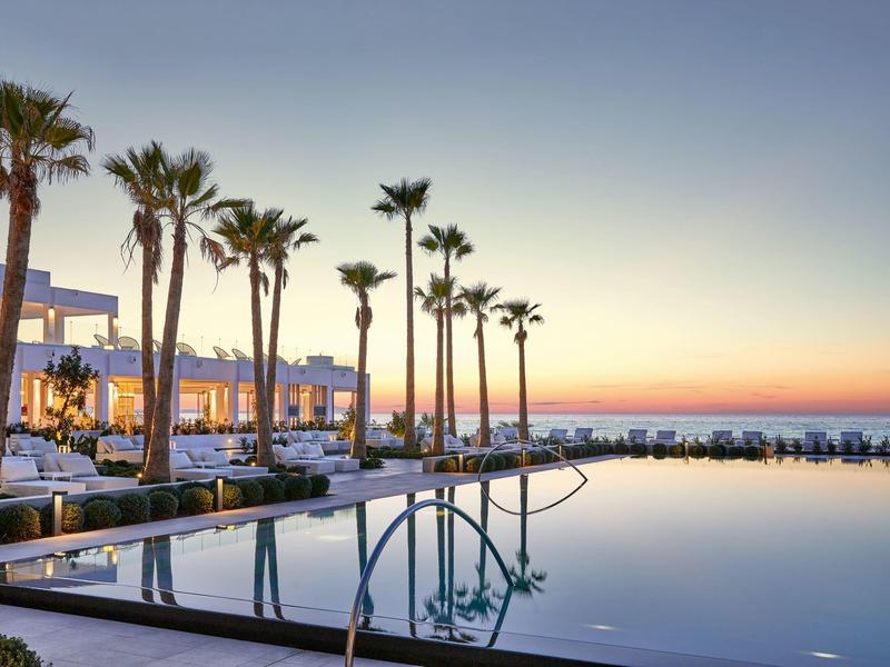 Nowoczesny basen z palmami o zachodzie słońca z widokiem na morze.