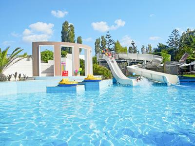 Una piscina grande con toboganes de agua y terraza soleada bajo un cielo azul.