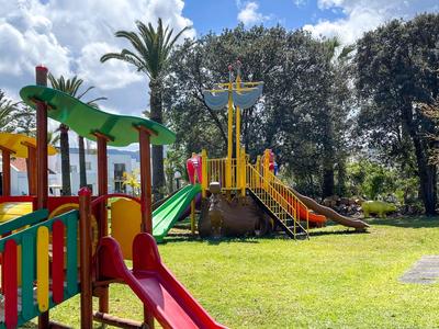 Área de juegos colorida con toboganes y estructuras para trepar en jardín de hotel tipo parque