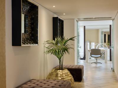 Vista a través de un pasillo luminoso del hotel con plantas y asientos hacia la recepción.