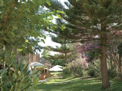 Giardino verde con ombrelloni e tavoli vicino a un edificio dell'hotel in una giornata di sole.