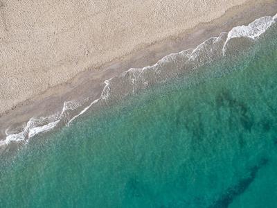 Vista aérea de una playa tranquila con agua azul verdosa clara y olas suaves.