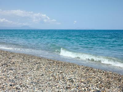 Playa de guijarros con olas suaves y cielo azul al fondo.