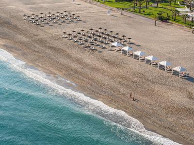 Plaża z rzędami leżaków i białych parasoli obok niebieskiego morza.