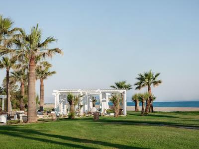 Zielony trawnik z palmami i białą pergolą nad morzem pod jasnym niebem.