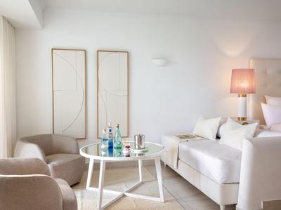 Soggiorno moderno con divani beige, tavolo rotondo bianco, bottiglie d'acqua e decorazioni murali minimaliste.