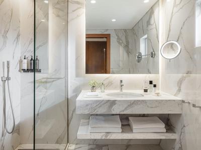 Bagno moderno in hotel con doccia in vetro, grande specchio e lavandino in marmo bianco.