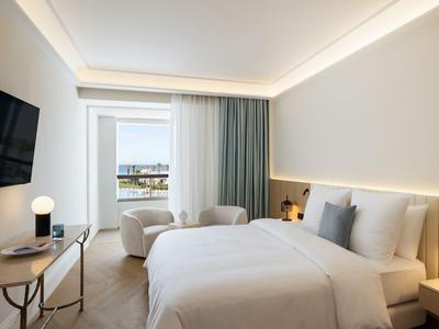 Camera d'albergo luminosa con letto matrimoniale, due poltrone e vista sul balcone.