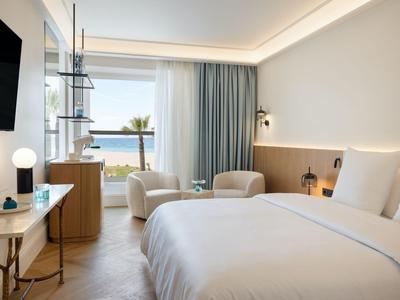 Camera d'hotel luminosa con letto matrimoniale, zona salotto e vista sul mare da grandi finestre.