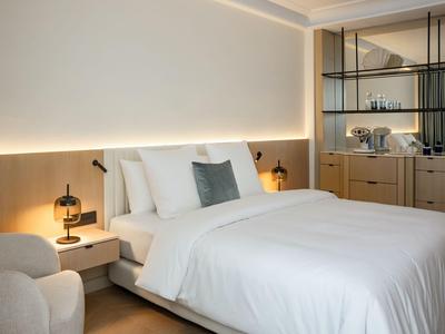 Camera d'hotel moderna con grande letto bianco, lampade da comodino e angolo salotto.