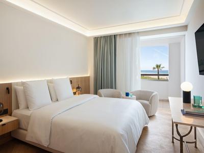 Camera d'hotel moderna con letto matrimoniale, zona salotto e vista sul mare.