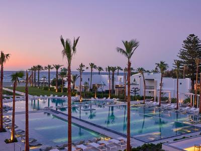 Piscina moderna dell'hotel con palme e lettini al tramonto vicino al mare.